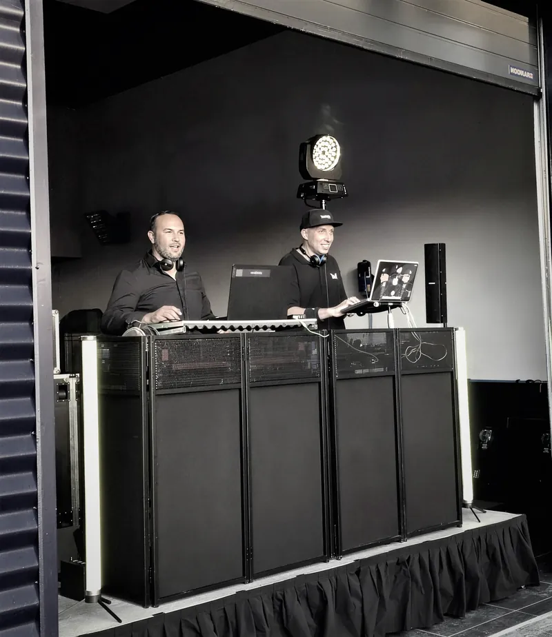 Façade DJ noire avec bandeaux lumineux jaunes, deux DJ derrière les platines