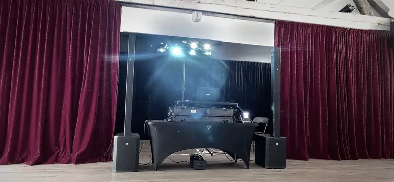 Scène aux rideaux rouges, enceintes de part et d’autre d’une table DJ noire